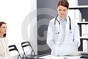 Happy doctor woman at work. Portrait of female physician using laptop computer while standing near reception desk at