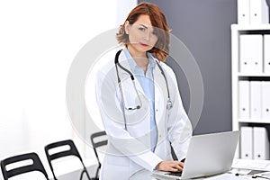 Happy doctor woman at work. Portrait of female physician using laptop computer while standing near reception desk at