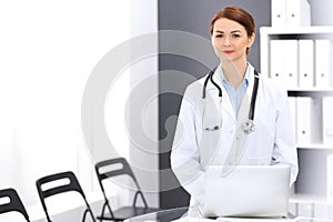 Happy doctor woman at work. Portrait of female physician using laptop computer while standing near reception desk at