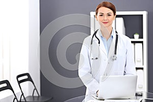 Happy doctor woman at work. Portrait of female physician using laptop computer while standing near reception desk at