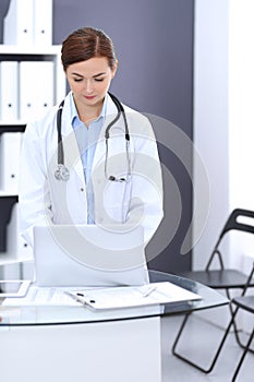 Happy doctor woman at work. Portrait of female physician using laptop computer while standing near reception desk at