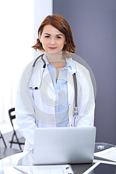 Happy doctor woman at work. Portrait of female physician using laptop computer while standing near reception desk at