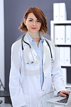 Happy doctor woman at work. Portrait of female physician using laptop computer while standing near reception desk at