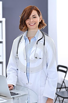 Happy doctor woman at work. Portrait of female physician using laptop computer while standing near reception desk at