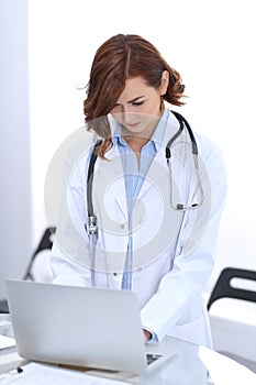 Happy doctor woman at work. Portrait of female physician using laptop computer while standing near reception desk at