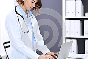 Happy doctor woman at work. Portrait of female physician using laptop computer while standing near reception desk at