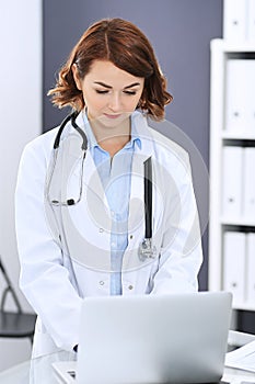 Happy doctor woman at work. Portrait of female physician using laptop computer while standing near reception desk at