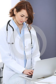 Happy doctor woman at work. Portrait of female physician using laptop computer while standing near reception desk at