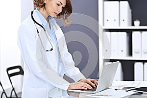 Happy doctor woman at work. Portrait of female physician using laptop computer while standing near reception desk at