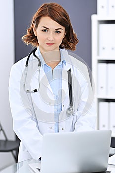 Happy doctor woman at work. Portrait of female physician using laptop computer while standing near reception desk at