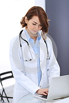 Happy doctor woman at work. Portrait of female physician using laptop computer while standing near reception desk at