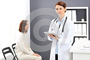 Happy doctor woman at work. Portrait of female physician using tablet computer while standing near reception desk at