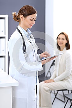 Happy doctor woman at work. Portrait of female physician using tablet computer while standing near reception desk at