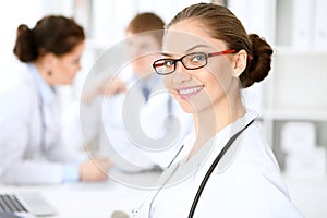 Happy doctor woman with medical staff at the hospital sitting at the table. Red frame glasses