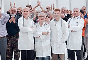 Happy doctors standing in corridor with team at hospital with crossed arms looking at camera