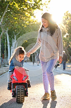 Happy Dominican mother playing with her son on a balance bike in a park.