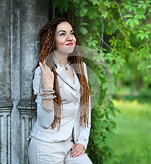 Happy dreadlocks fashionable girl posing near old column and trees