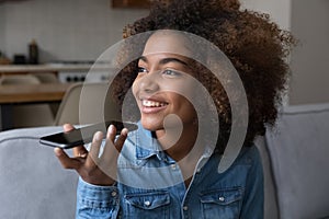 Happy dreamy African girl talking on mobile phone on speaker