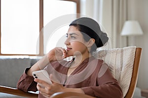 Happy dreamy indian woman resting with cellphone in hands.