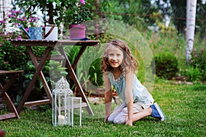 Happy dreamy kid girl playing in summer garden, decorated with lantern light and candle