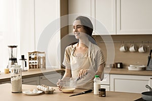 Happy dreamy pretty young woman cooking homemade breakfast in kitchen