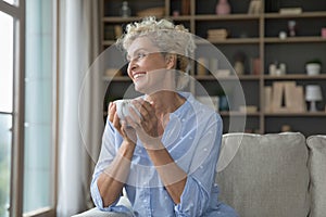 Happy dreamy senior woman holding mug of hot drink