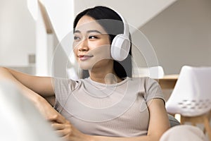 Happy dreamy young Asian woman in wireless headphones looking away