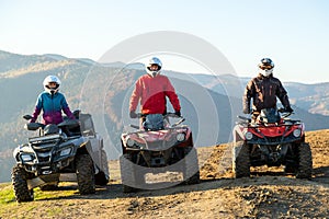 Happy drivers in protective helmets enjoying extreme ride on ATV quad motorbikes in fall mountains at sunset