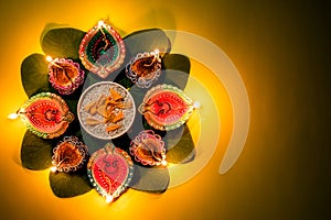 Happy Dussehra. Clay Diya lamps lit during Dussehra with yellow flowers, green leaf and rice on yellow pastel background. Dussehra