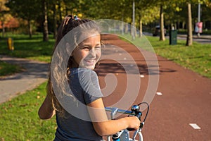 Happy dutch kid laughs. Beautiful little girl rides bike on bike path. Cyclist child or teenager girl enjoys good weather and