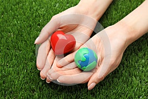 Happy Earth Day. Woman with plasticine planet and decorative heart on green grass, closeup