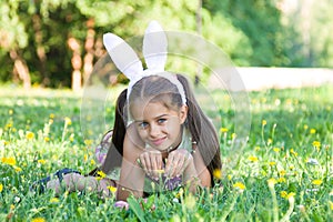 Happy Easter: adorable little girl wearing bunny ears lying on the grass outdoors