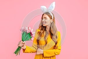 Happy Easter. Happy woman in Easter Bunny ears, girl with a bouquet of tulips, on an isolated pink background