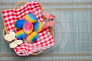 Happy easter background. Top view of colorful easter eggs in a basket on red checkered napkin on a green bamboo mat. Space for