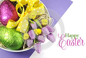 Happy Easter basket of colorful pink and green foil wrapped eggs and pink purple tulips with chicks