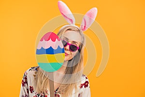 Happy Easter - a blonde young woman with Easter bunny ears holding a big wooden Easter egg holiday concept orange