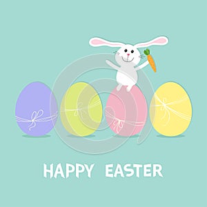 Happy Easter bunny. Rabbit with carrot sitting on painting egg shell set. Painted eggs with thread and bow. Farm animal. Cute cart