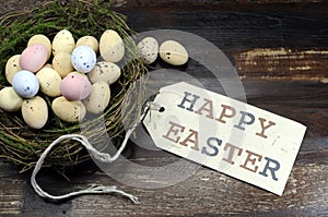 Happy Easter candy easter eggs in birds nest on dark vintage recycled wood with tag