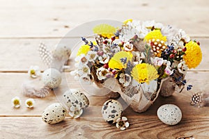 Happy Easter card with colorful flowers, feather and quail eggs on rustic wooden background. Beautiful spring composition.