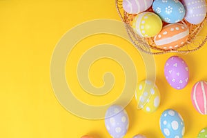 Happy easter celebration holiday. colourful pastel painted eggs in wicker basket nest decoration on a yellow background. Seasonal