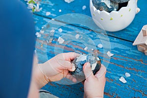 Happy easter. Children& x27;s hands clean Easter egg on blue wooden background