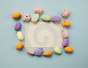 Happy Easter composition with Easter colored eggs and paper blank on a pastel blue background. Flat lay, top view, copy space.