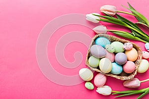 Happy Easter composition. Easter eggs in basket on colored table with yellow Tulips. Natural dyed colorful eggs