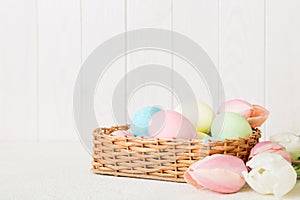 Happy Easter composition. Easter eggs in basket on colored table with yellow Tulips. Natural dyed colorful eggs