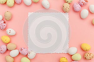 Happy Easter concept. Candy chocolate eggs and jellybean sweets with mockup empty poster isolated on pastel pink