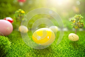 Happy Easter concept. Colorful easter eggs and one big yellow easter egg on spring green grass. Fairy tale sunset on the plastic g