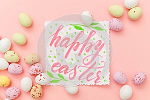 Happy Easter concept. Inscription HAPPY EASTER letters candy chocolate eggs and jellybean sweets isolated on trendy pastel pink