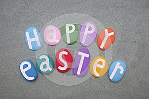 Happy Easter, creative celebration with multi colored stone letters over green sand
