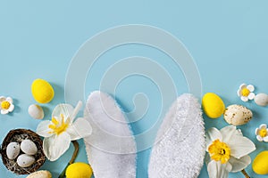 Happy Easter! Easter eggs, bunny ears and daffodils flowers flat lay on blue background. Stylish festive template with space for