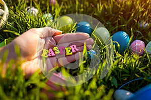 Happy Easter. Easter eggs hidden in spring grass. Writing made of wooden letters in hand